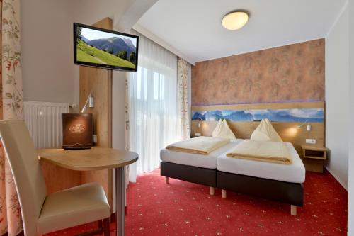 a hotel room with a bed and a desk and a television at Hotel Alpenhof in Westendorf