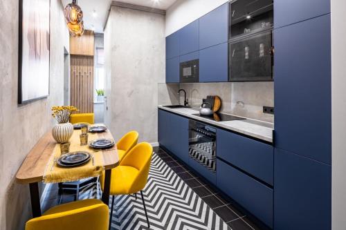 eine Küche mit blauen Schränken, einem Tisch und gelben Stühlen in der Unterkunft Куліша 12 in Lwiw