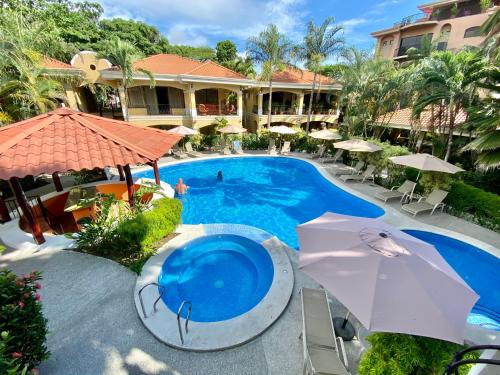 uma piscina num resort com guarda-sóis e cadeiras em Monte Carlo Luxury Condominiums em Jacó