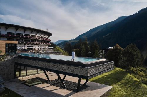 une personne debout au bord d'une piscine dans un complexe dans l'établissement Travel Charme Ifen Hotel Kleinwalsertal, à Hirschegg