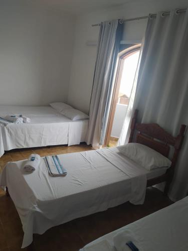 two beds in a room with a window at Hotel Haloha in Peruíbe