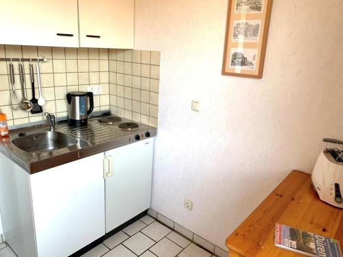 cocina con armarios blancos, fregadero y mesa en Appartementhaus Schlagstein App1 en Kreuzau