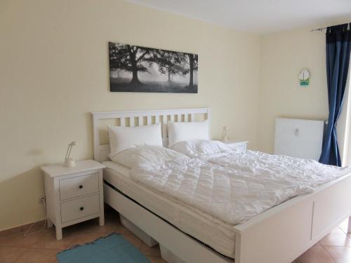 a bedroom with a white bed and a night stand at Lindenstraße 43, Whg 1 - Nord bei Nordost in Zingst