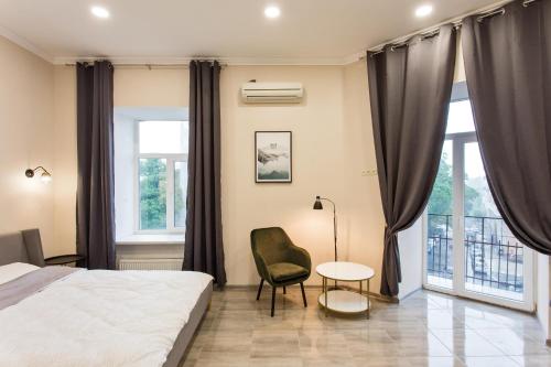 a bedroom with a bed and a chair and windows at Havana ApartHotel in Odesa