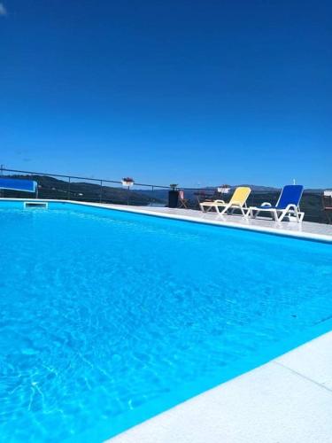 a blue swimming pool with two chairs and the ocean at Vivenda das Carvalhas in Amiar