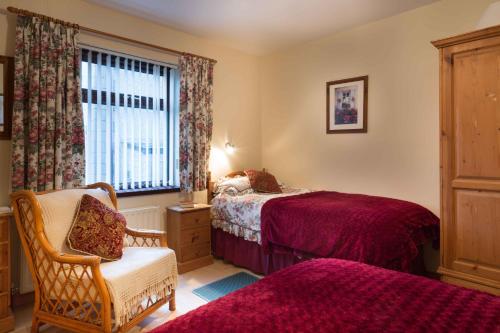 a bedroom with two beds and a chair and a window at Drumgart Self Catering Cottage in Carrickfergus