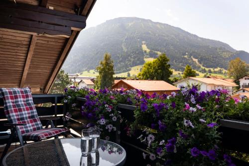 einen Tisch und Stühle auf einem Balkon mit lila Blumen in der Unterkunft Hotel Garni Bergidyll - adults only in Pfronten