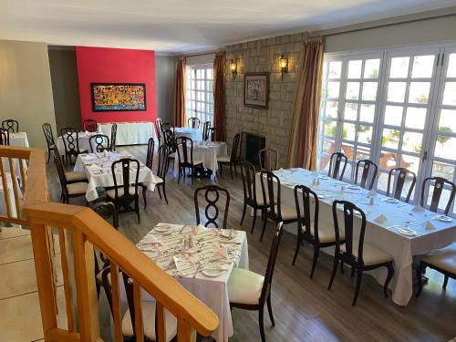 a dining room with white tables and chairs and windows at The Historic Hogsback Inn in Hogsback