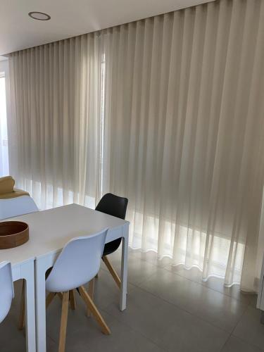 a white table and chairs next to a window with curtains at Slow House d'Arco in São Brás de Alportel