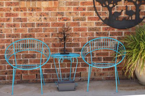 two blue chairs and a table in front of a brick wall at All Settlers Motor Inn Parkes in Parkes