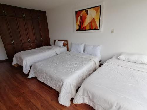 three beds in a room with white sheets at Hotel Paipa Inn in Paipa