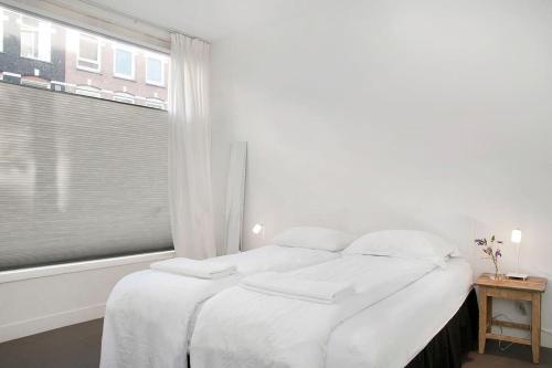 een witte slaapkamer met een bed en een raam bij The Little Townhouse in Amsterdam