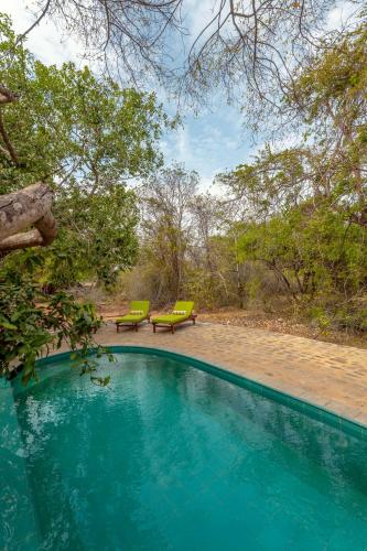 a swimming pool with two green benches and trees at Leopard Safaris Yala in Yala