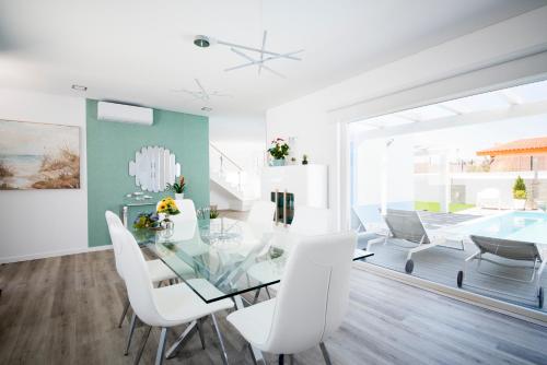 a dining room with a glass table and white chairs at Casa da Praia & Casa da Mare da Alta by Estilo Lusitano, com piscina privada in Porto Covo