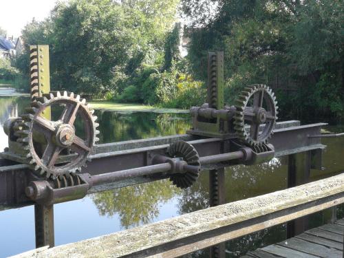 a wooden bridge with gears on the side of a river at Pension Schlossblick Thallwitz in Thallwitz