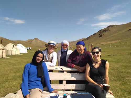 a group of people sitting on a bench in a field at Yurt Camp Azamat at Song Kol Lake in Bagysh