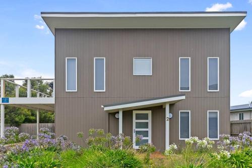 a brown house with white windows and bushes at Charlie’s Beach House 1Block to Beach Pet Friendly in Apollo Bay