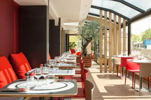 a row of tables in a restaurant with red chairs at ibis Paris Gennevilliers in Gennevilliers