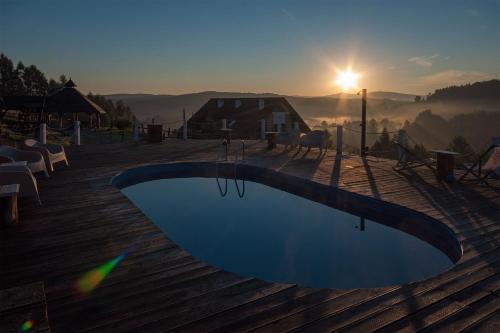 a swimming pool on a deck with the sunset in the background at Chata w Bieszczadzie apartamenty i domki z basenem Bieszczady in Polańczyk