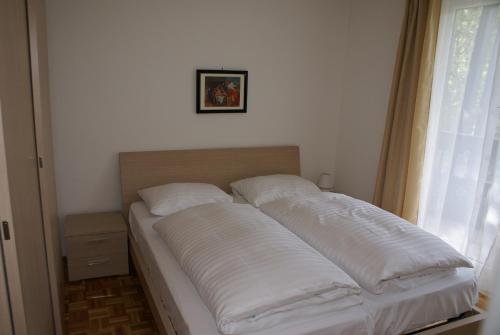 Bett mit weißen Kissen in einem Zimmer mit Fenster in der Unterkunft Appartementanlage Bach in Bad Kleinkirchheim