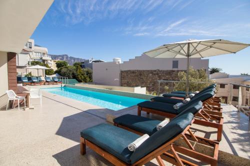 un grupo de tumbonas y una sombrilla junto a la piscina en Village Apartments - Camps Bay, en Ciudad del Cabo