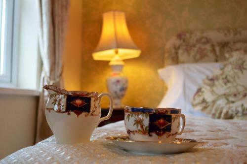 two cups and a plate on a table next to a bed at Killyliss Country House B&B in Lisnalong