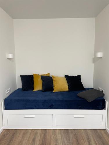 a white bed with blue and yellow pillows on it at Forest Studio in Druskininkai