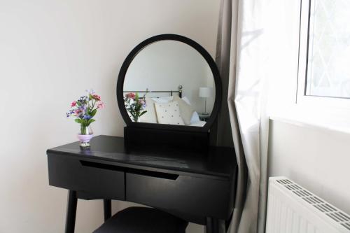 a black vanity with a mirror and a vase of flowers at Oxford - Private House with Garden & Parking 05 in Oxford