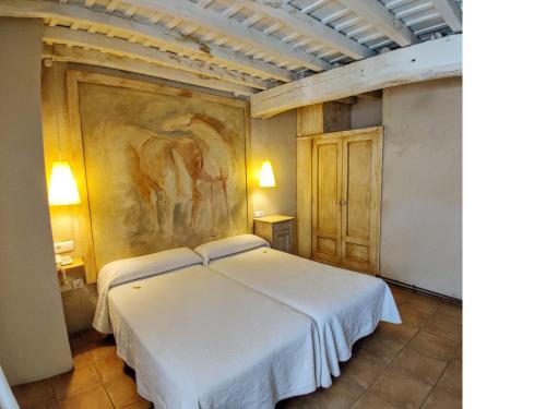 a bedroom with a white bed with a painting on the wall at Posada Restaurante Casa de la Sal in Candelario
