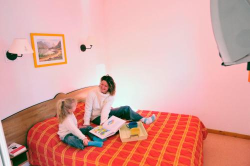 two girls sitting on a bed reading a book at Résidence Goélia - Le Rond Point des Pistes in Saint-François-Longchamp