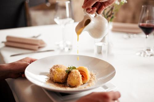 a person pouring sauce onto a plate of food at Hotel Gasthaus Post in Campo di Trens
