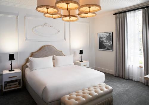 Habitación blanca con cama grande y lámpara de araña. en The Alphen Boutique Hotel & Spa en Ciudad del Cabo