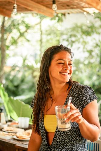 a woman is smiling while holding a glass at Akih Pods Hostel in Santa Teresa Beach