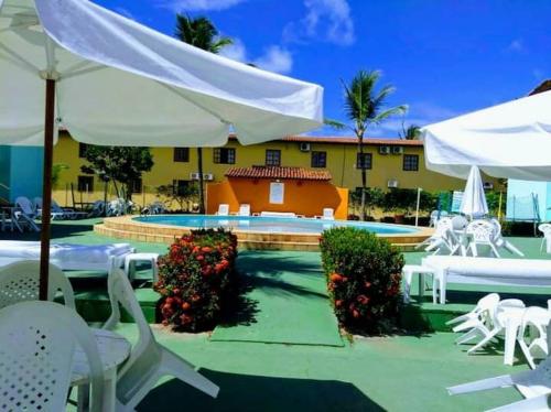 Un complejo con piscina, mesas blancas y sombrillas. en Apartamento Taperapuã Praia Vilage, en Porto Seguro
