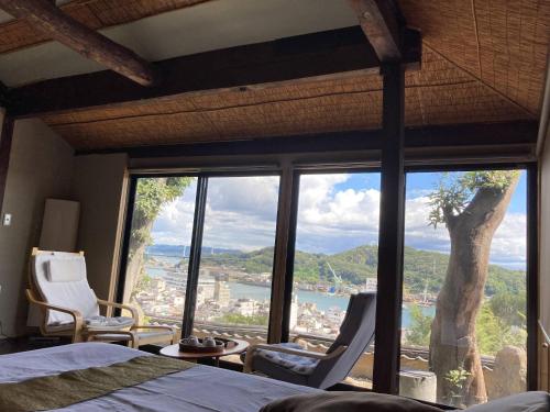 a bedroom with a bed and chairs and a large window at Onomichi Senkouji Sakano Rian Fuu in Onomichi