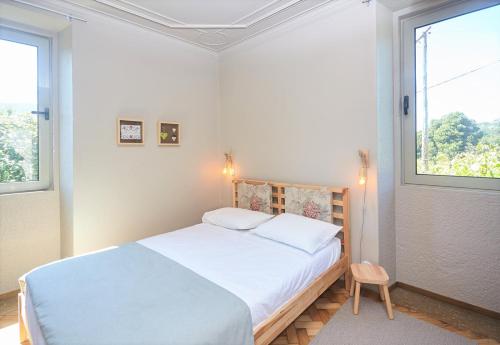 a white bedroom with a bed and two windows at Casa da Oliveira in Caminha
