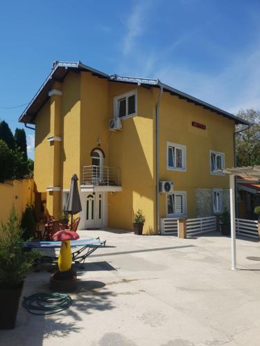 a yellow house with a table and an umbrella at Comfort Inn Apartmani in Vrnjačka Banja
