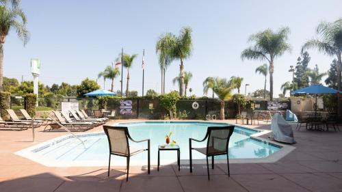 a pool with two chairs and a table with a drink at Holiday Inn Santa Ana-Orange Co Arpt by IHG in Santa Ana