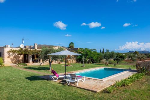 a woman sitting under an umbrella next to a swimming pool at Ca Sa Padrineta in Capdepera