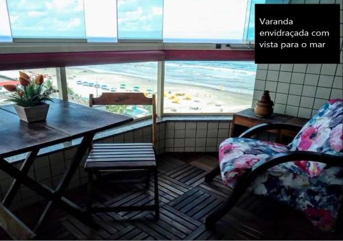 a table and a chair in a room with a view of a beach at Mongaguá - Pé na Areia - 2 Quartos - 6 pessoas in Mongaguá