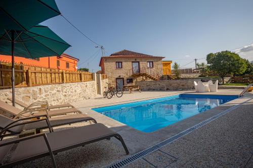 a pool with chairs and an umbrella and a house at Casa da Clarinha, piscina, perto Sistelo e Ecovia do Vez in Arcos de Valdevez