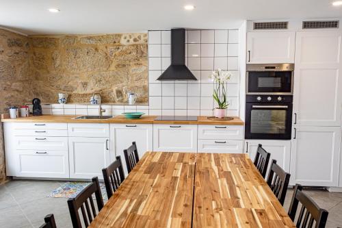 a kitchen with white cabinets and a wooden table with chairs at Casa da Clarinha, piscina, perto Sistelo e Ecovia do Vez in Arcos de Valdevez