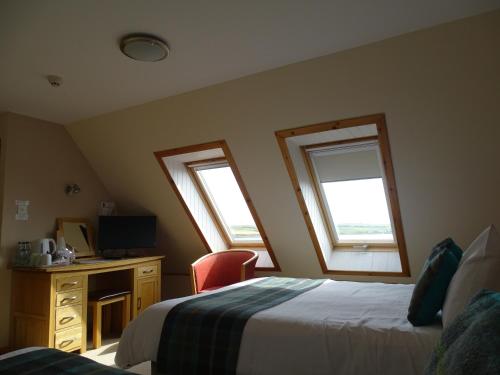 a bedroom with two beds and a desk and two windows at The Sands Hotel, Orkney in Burray Village
