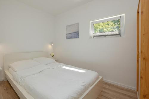 a white bedroom with a bed and a window at Baltic Center Bungalows in Sarbinowo