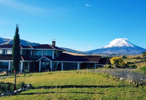 a house in a field with a mountain in the background at Balcon al Cotopaxi Hosteria in Sangolquí