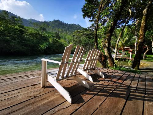 zwei Holzstühle auf einem Steg neben einem Fluss in der Unterkunft Hostal Oasis The Traveler in Lanquín