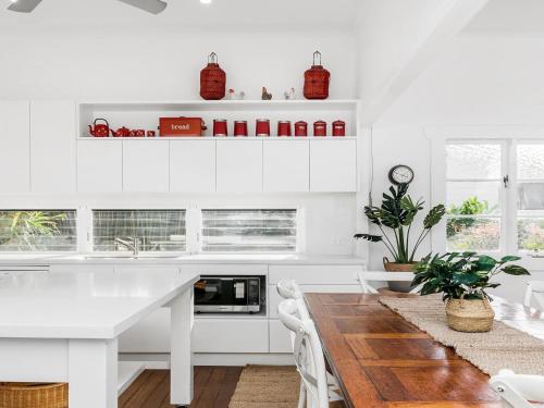 a kitchen with white cabinets and a wooden table at Alkira - Boutique cottage - Walk to Clarkes Beach in Byron Bay