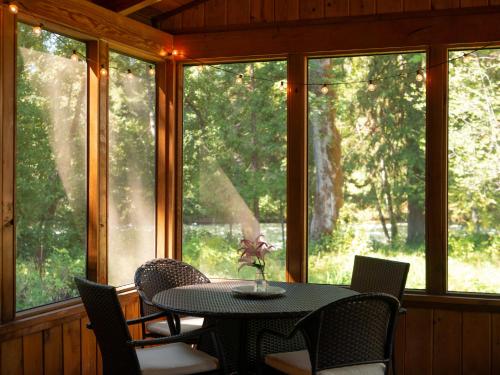 a table and chairs in a room with windows at On the River Wooded Bliss Cabin near Loloma in McKenzie Bridge