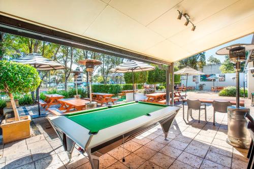 a pool table on a patio with tables and umbrellas at Nightcap at High Flyer Hotel in Bankstown