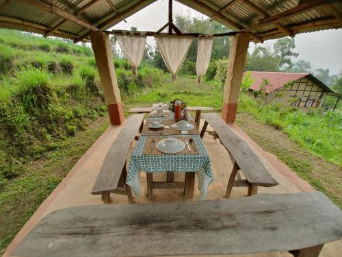 una larga mesa de madera con bancos y platos. en PaliGhar Farmstay, en Kalimpong